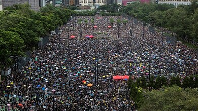 Large crowd of protesters in Hong Kong rally with umbrellas and banners.