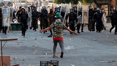 Young protester faces riot police with shields during Iraq protests.