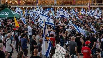 Large crowd of Israelis protesting with flags and banners in support of Netanyahu.