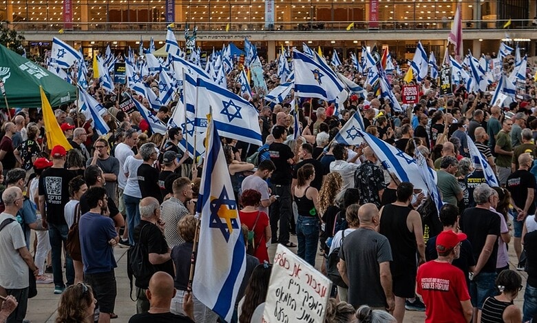 Large crowd of Israelis protesting with flags and banners in support of Netanyahu.