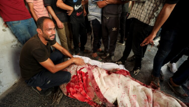 Palestinians stand next to the body of a martyr after an Israeli airstrike on a school housing displaced people in Gaza