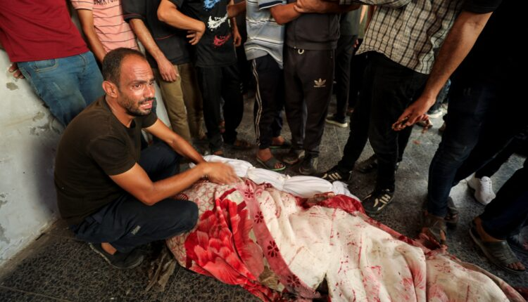 Palestinians stand next to the body of a martyr after an Israeli airstrike on a school housing displaced people in Gaza