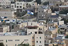 Israeli flag flying above a crowded urban area with closely built houses and rooftops.