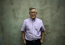 Man smiling in front of a plain wall.