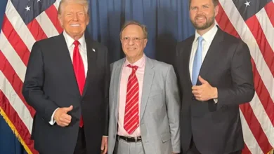 Donald Trump with two men at a political event, posing in front of American flags.