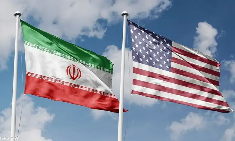 Iran and US flags flying side by side against a blue sky.