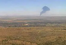 Large plume of black smoke rising in desert after aircraft crash.