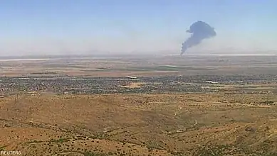 Large plume of black smoke rising in desert after aircraft crash.