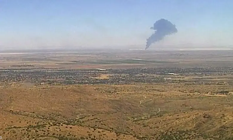 Large plume of black smoke rising in desert after aircraft crash.