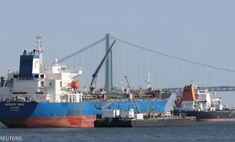 Cargo ships docked at a port with a bridge in the background.